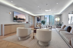 A modern living room with a flat-screen TV, a sofa, a coffee table, and a large window with a view of high-rise buildings. - 501-705 Luxury Corner 1 Bedroom Rooftop Pool & GYM (Miami)