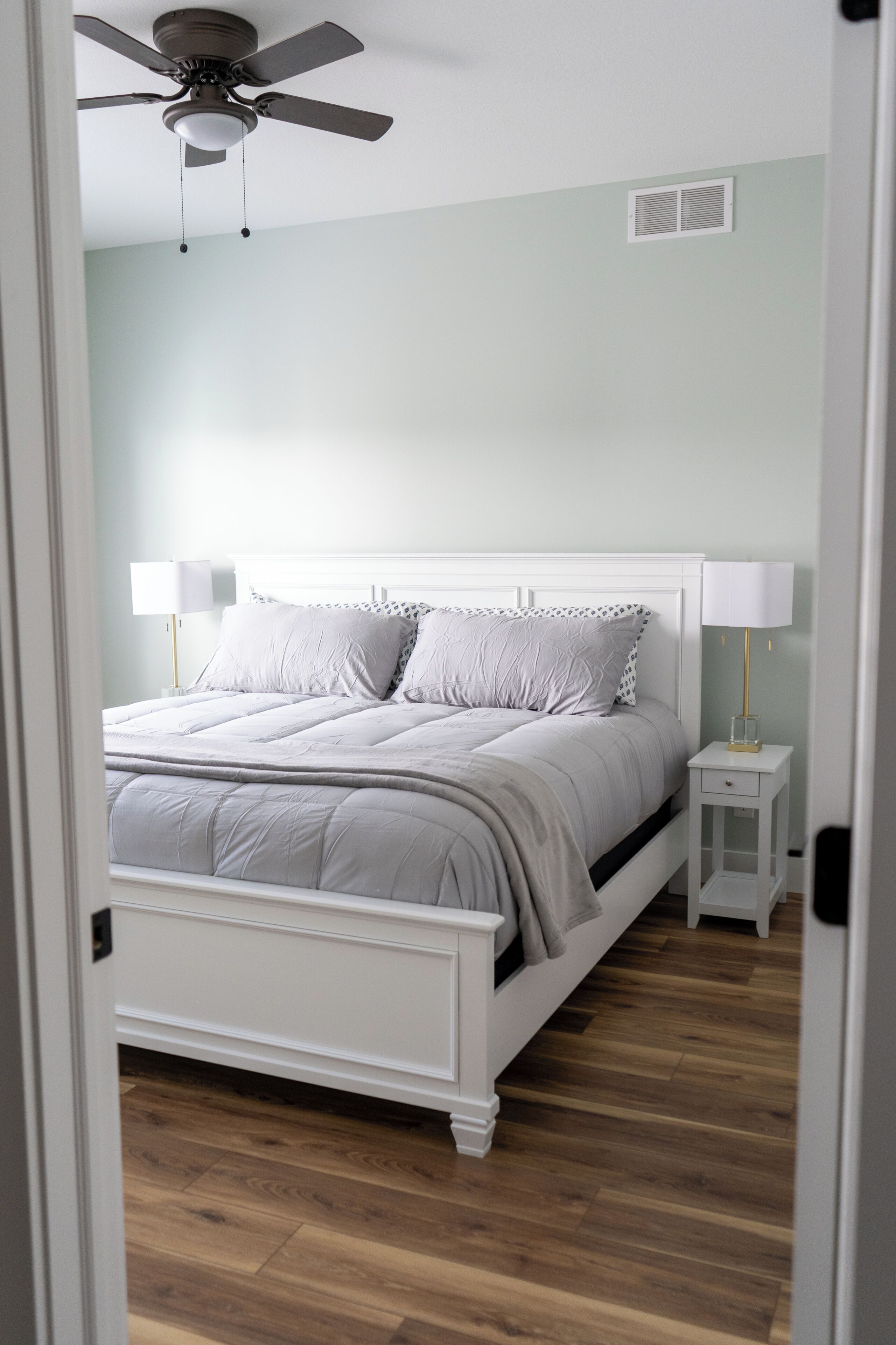 A bedroom with a bed, bedside tables, a ceiling fan, and a wall vent.