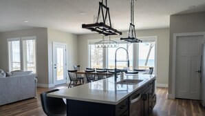 A modern kitchen with a large island, black bar stools, and a view of the ocean through large windows.