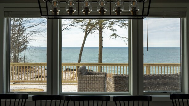 A room with large windows overlooking a beach, wicker furniture, and a ceiling light fixture.