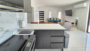 Una cocina moderna con horno integrado, un comedor con encimera de mármol y una sala de estar con sofá y televisor.