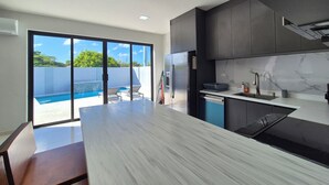Una cocina moderna con una isla grande, muebles oscuros y vistas a una piscina.