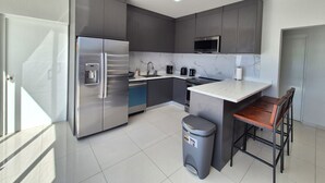 Una cocina moderna con gabinetes grises, electrodomésticos de acero inoxidable, salpicadero de mármol y una pequeña isla con taburetes de bar.