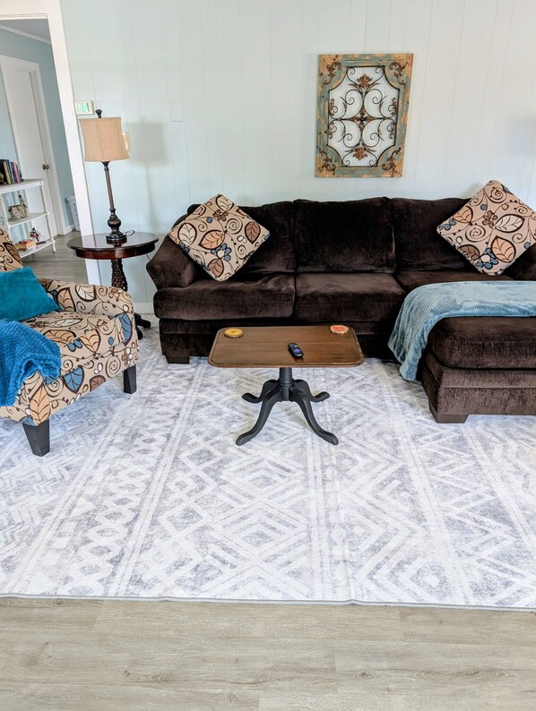 A living room with a brown sofa, patterned armchair, and ottoman, a coffee table, and a patterned rug. - Cabin with Saluda River access (Honea Path)
