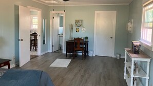 Ein Zimmer mit Deckenventilator, einem Esstisch mit Stühlen, einem kleinen weißen Regal mit Dekorationen und einem Fenster mit Jalousien.