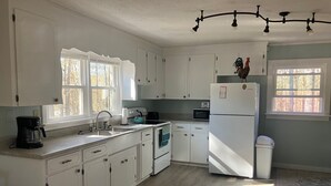Eine Küche mit weißen Schränken, einem Kühlschrank, einer Mikrowelle, einer Kaffeemaschine und einem Spülbecken.