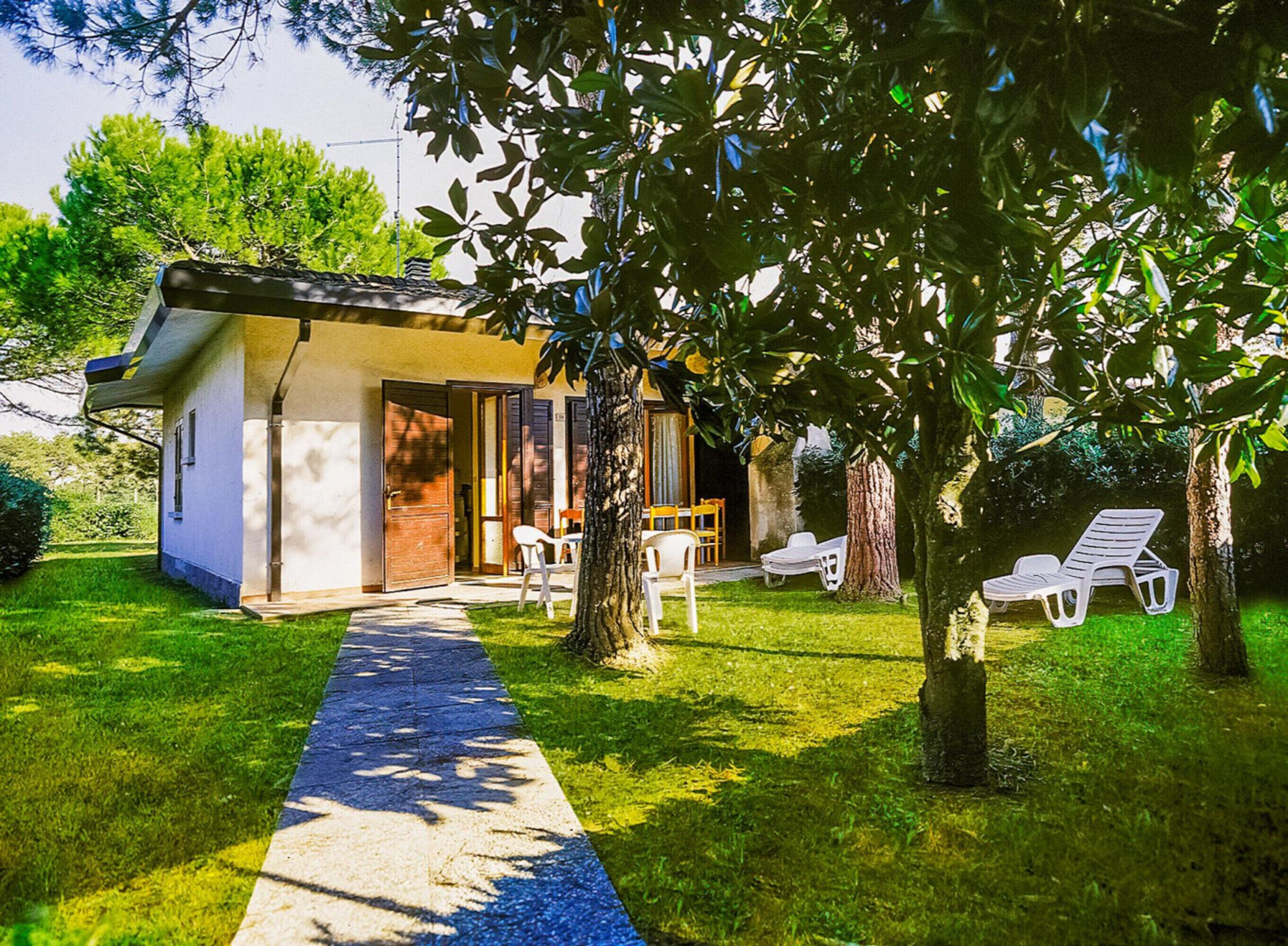 A small, single-story building with a paved pathway leading to a door. There are two outdoor seating areas with chairs and tables.
