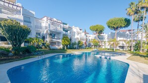 A swimming pool surrounded by white buildings with balconies, palm trees, and a clear blue sky. - Beachside Penthouse With Rooftop Terrace (Estepona)