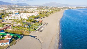 An aerial view of a coastal area with a beach, a hotel complex, and mountains in the background. - Beachside Penthouse With Rooftop Terrace (Estepona)
