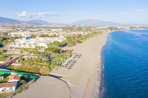 An aerial view of a coastal area with a beach, a hotel complex, and mountains in the background. - Beachside Penthouse With Rooftop Terrace (Estepona)