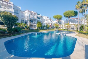 A swimming pool with a curved edge, surrounded by a paved area, and adjacent to white buildings with balconies and greenery. - Beachside Penthouse With Rooftop Terrace (Estepona)