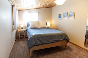 A bedroom with a wooden bed frame, a nightstand, a lamp, and a window with curtains.