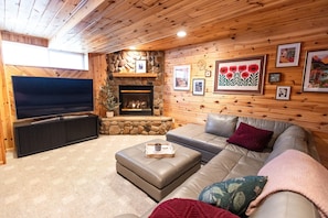 A cozy living room with a stone fireplace, a flat-screen TV, a leather sofa, and a coffee table.