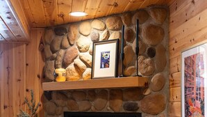 Una chimenea de piedra con repisa de madera, un cuadro enmarcado y un pequeño árbol en maceta.