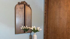 Una consola de madera con un jarrón de flores blancas, dos otomanas de cuero marrón y un espejo con un marco ornamentado.