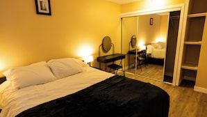 A hotel room with a bed, a desk with a chair, a mirror, and a wardrobe. - Charming 2-bedroom House in Central Calgary (Calgary)