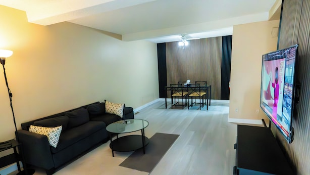 A modern living room with a black sofa, a glass coffee table, and a flat-screen TV mounted on the wall. - Charming 2-bedroom House in Central Calgary (Calgary)