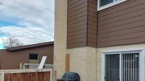 An outdoor patio area with a table and chairs, a barbecue grill, and a sliding glass door. - Charming 2-bedroom House in Central Calgary (Calgary)