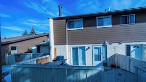 A two-story residential building with a wooden deck, a chimney, and a garage. - Charming 2-bedroom House in Central Calgary (Calgary)