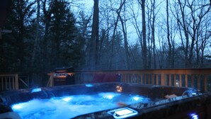 Un jacuzzi rodeado por una terraza de madera y un área boscosa.