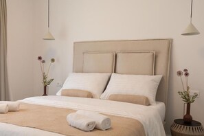 Ein ordentlich bezogenes Bett mit einem beigefarbenen Kopfteil, weißer Bettwäsche und zwei Nachttischen mit Blumenvasen.