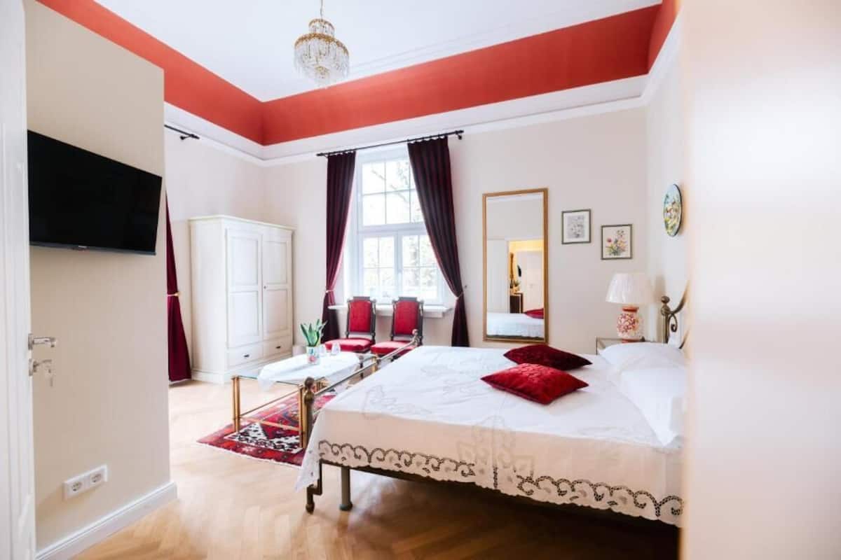 Une chambre à coucher avec un lit, un bureau, une chaise, un téléviseur et une fenêtre avec des rideaux.