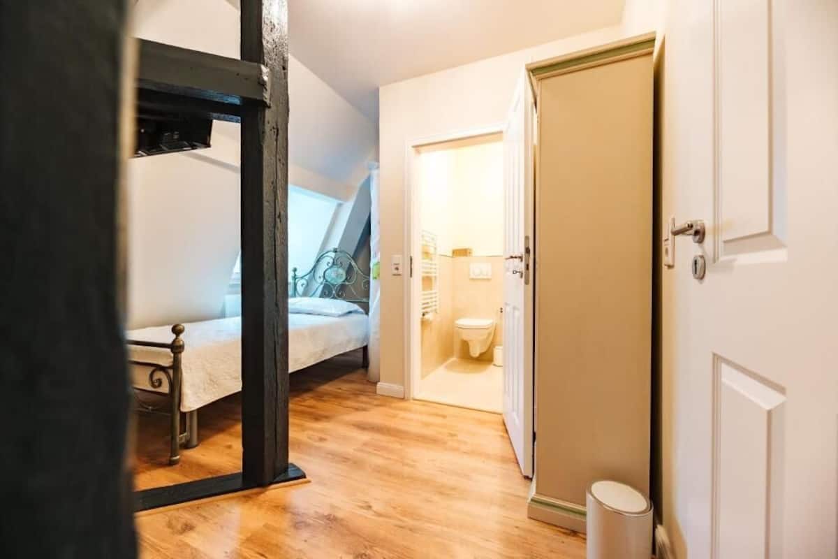 Une chambre à coucher avec un lit, un plancher en bois, une salle de bain avec des toilettes et un lavabo, et une porte.