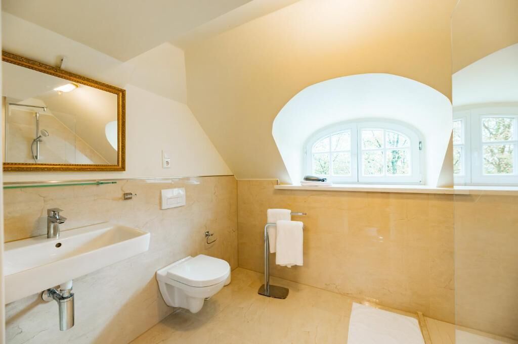 A bathroom with a large mirror, a sink, a toilet, and a window with a view of trees.