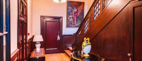 Un pasillo con puerta de madera, candelabro, un cuadro y una mesa con un jarrón.