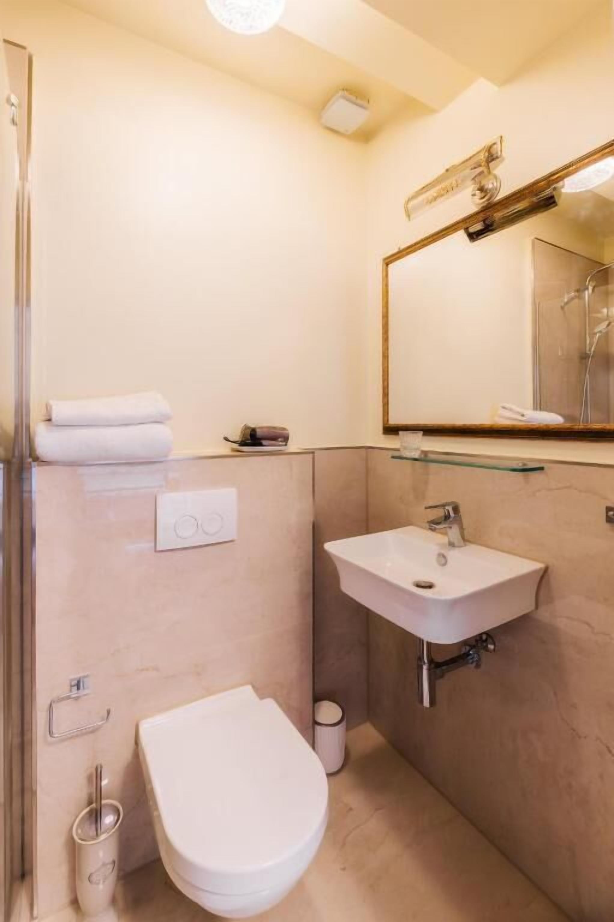 A compact bathroom with a toilet, sink, and a glass shelf above the sink.