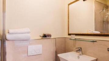 A compact bathroom with a toilet, sink, and a glass shelf above the sink.