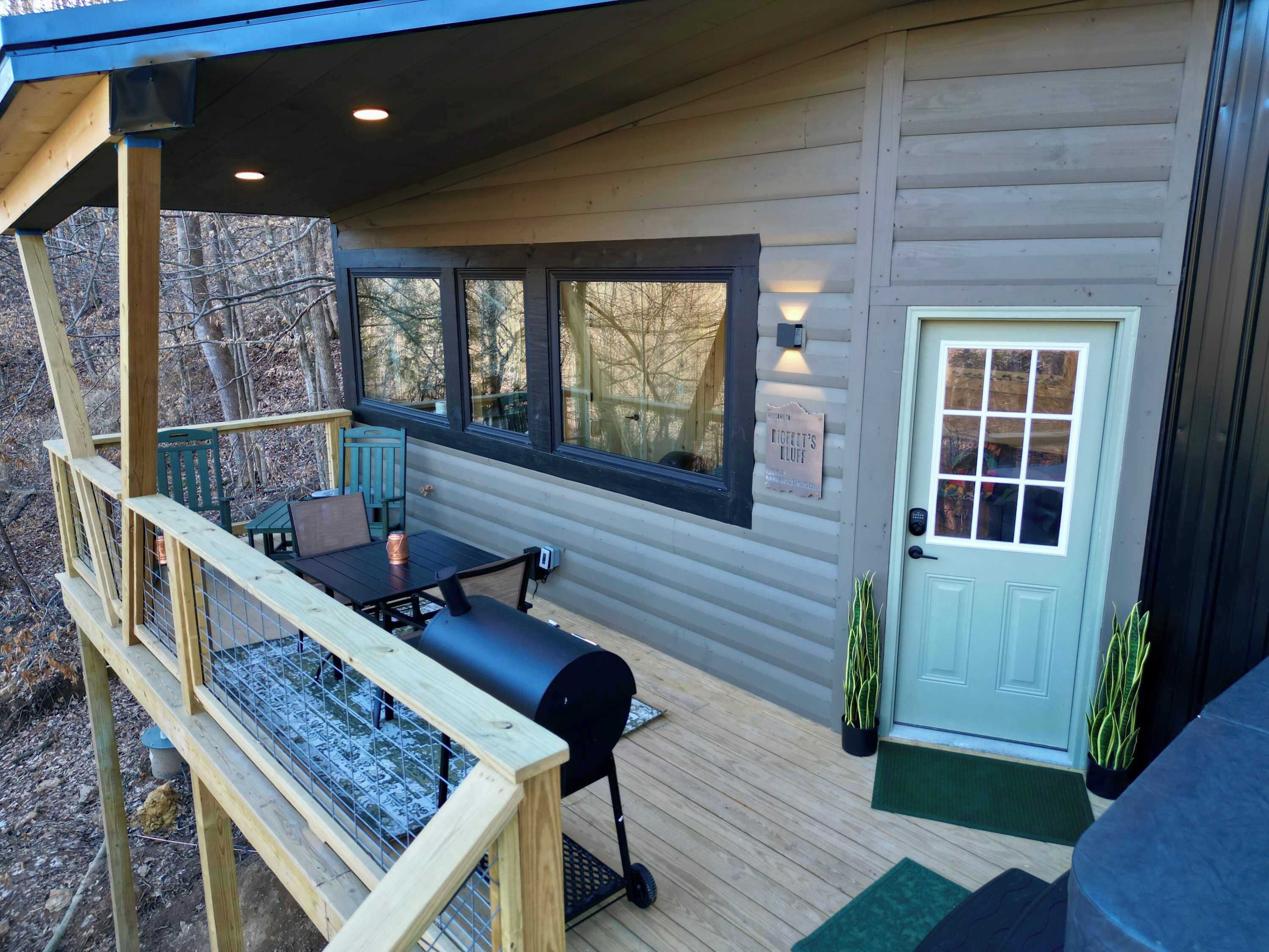 Eine Holzhütte mit einer Terrasse, einem Grill und einer Tür mit Fenster.
