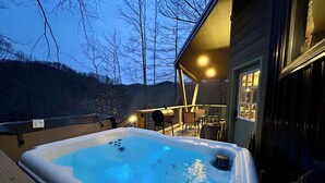 Ett bubbelbad på ett trädäck med utsikt över träd och en byggnad i bakgrunden.