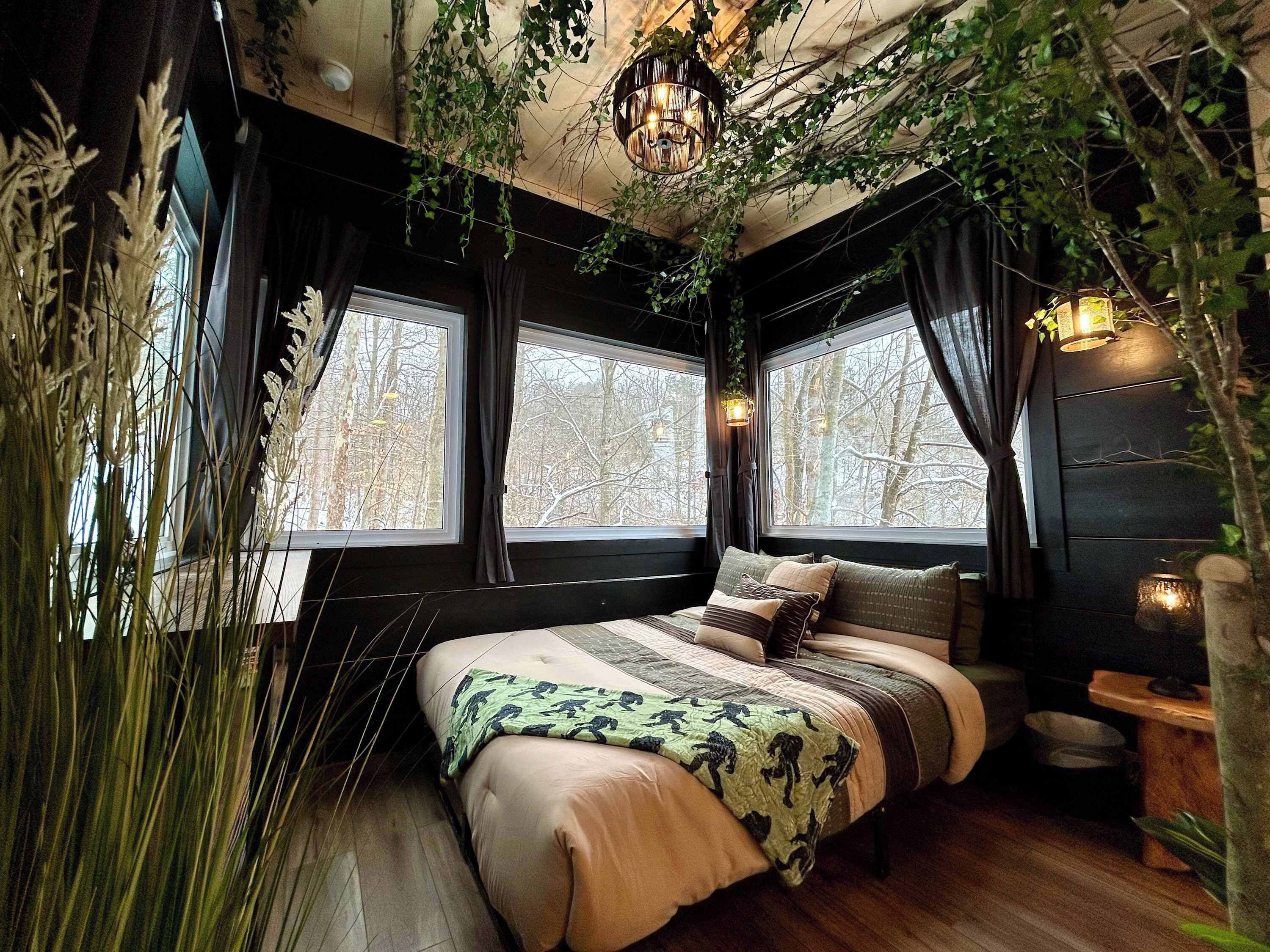 Une chambre confortable avec un grand lit, deux fenêtres et des plantes suspendues.