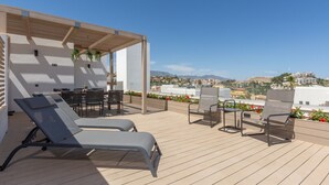 Eine Dachterrasse mit Liegestühlen und einer Pergola, mit Blick auf eine Küstenstadt.