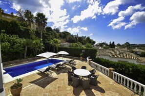 Ein Poolbereich mit gefliestem Patio, Liegestühlen und Sonnenschirmen.