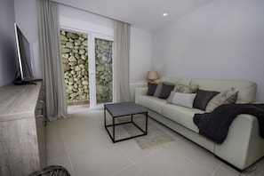 A modern living room with a sofa, a coffee table, a TV, and a stone wall. - Tranquil Sea View Villa for 8 (Marbella)
