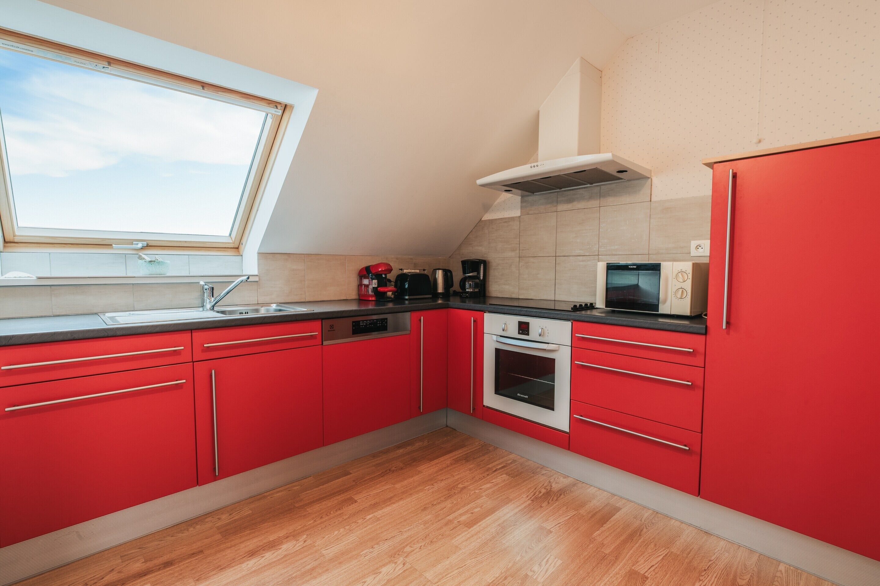 Une cuisine moderne avec des meubles rouges, un plan de travail noir, un four encastré, un four à micro-ondes et une fenêtre au-dessus de l’évier.