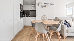 A modern kitchen with white cabinets, a dining table with chairs, and a decorative fish wall art piece. - Modern 3-pax Apartment With Solarium (Casares)