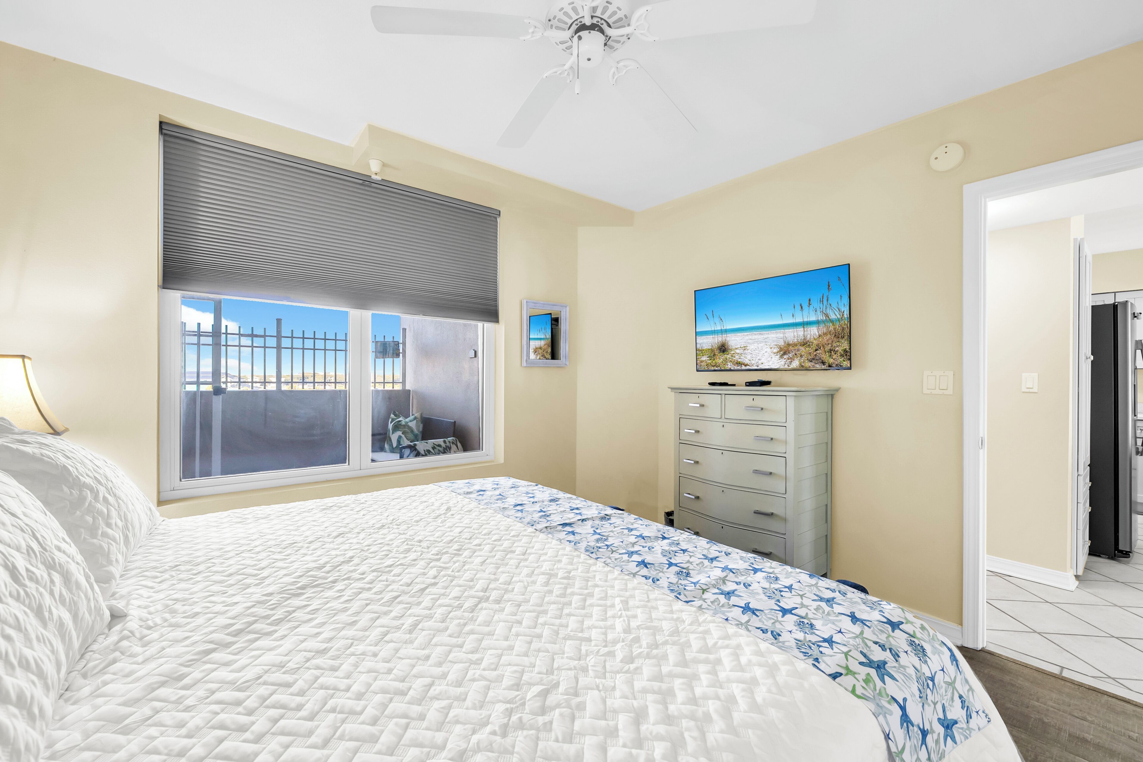 A bedroom with a bed, a dresser, a ceiling fan, a window with blinds, and a painting on the wall.
