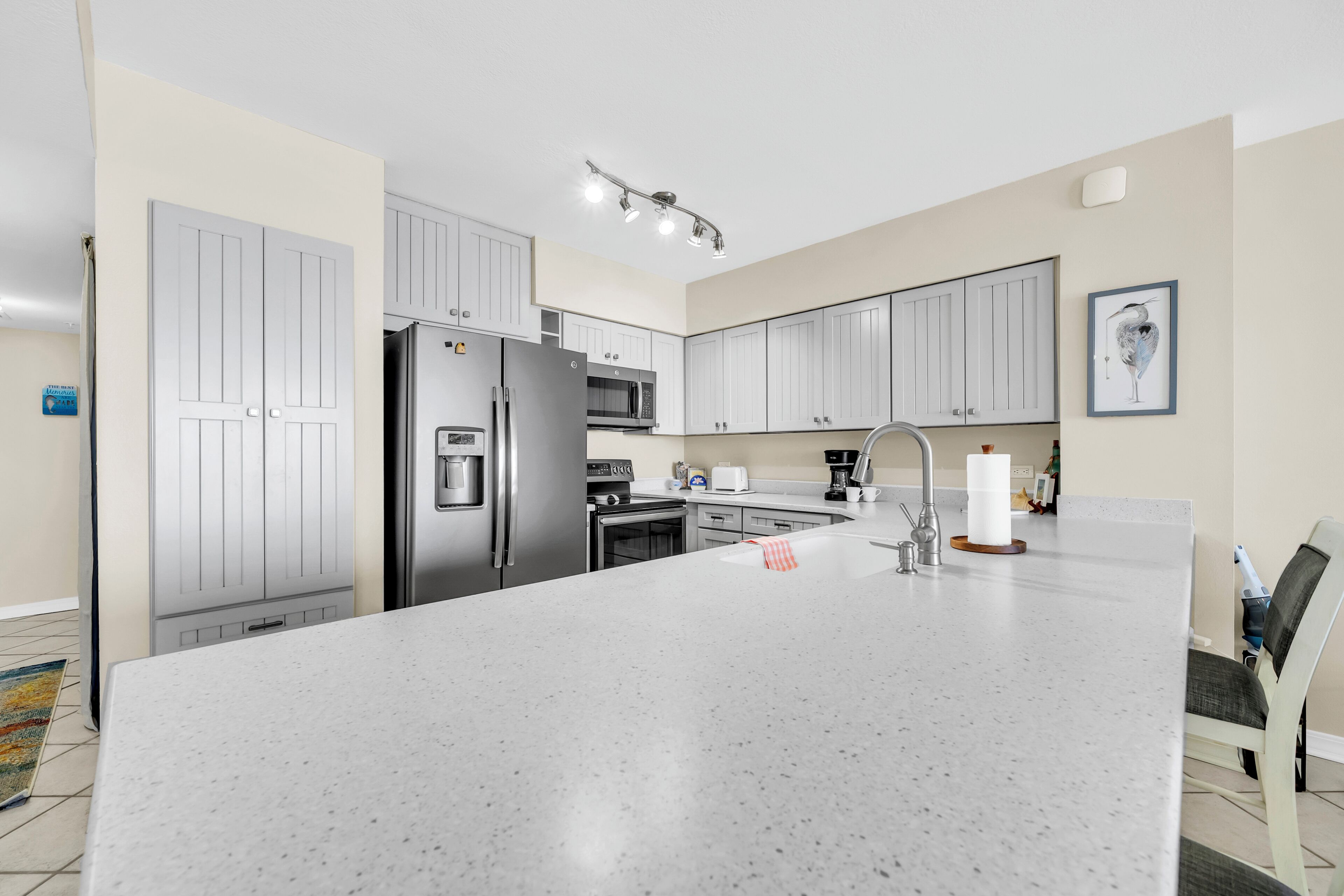 A modern kitchen with white cabinetry, stainless steel appliances, a large island, and a dining area with a chair.