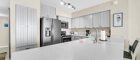 A modern kitchen with white cabinetry, stainless steel appliances, a large island, and a dining area with a chair.