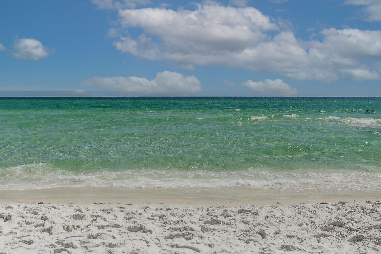 Una playa con agua turquesa cristalina, orilla de arena blanca y cielo parcialmente nublado.