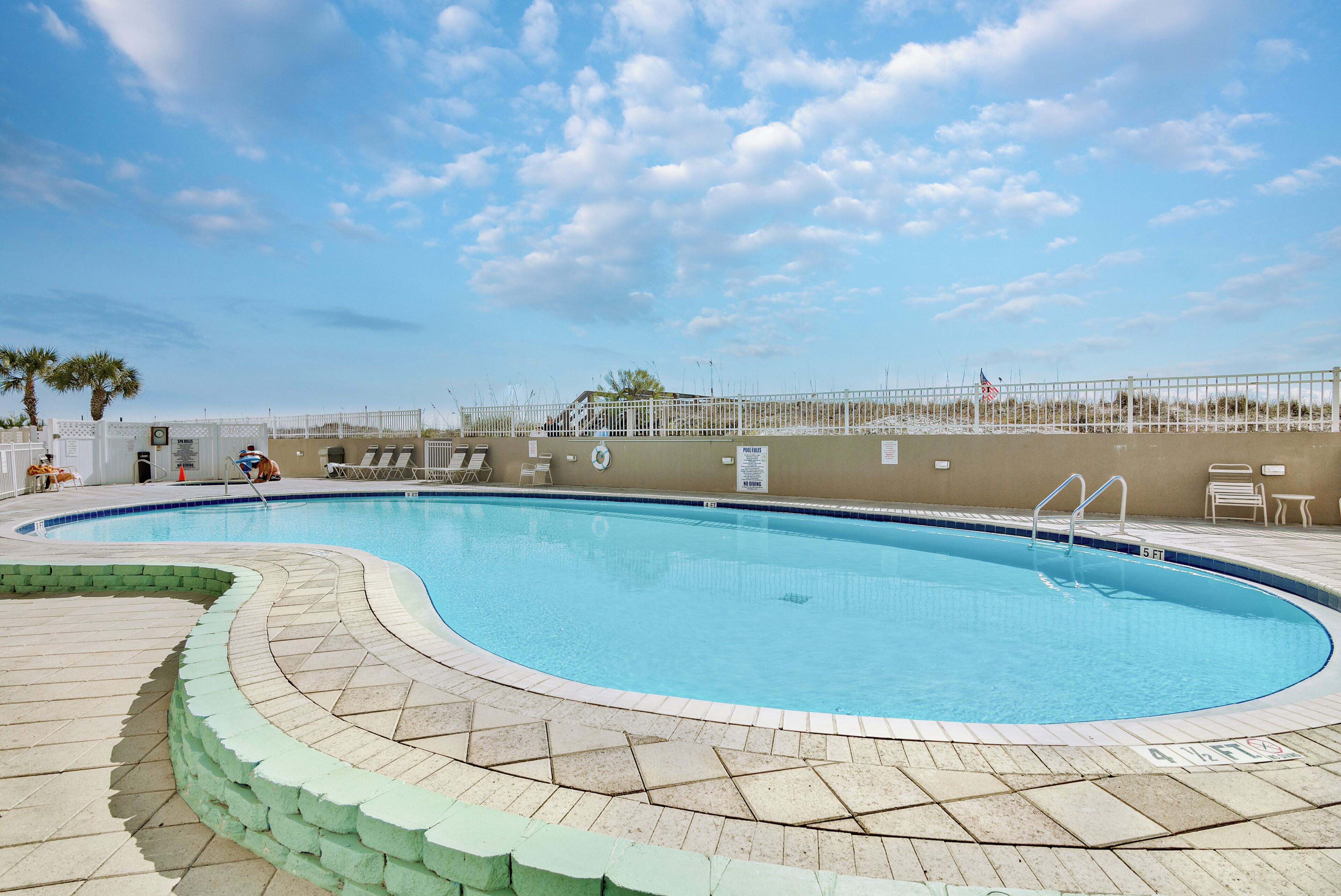 A swimming pool with a tiled deck, a fence, and a flag.