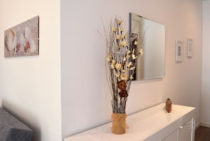 Een modern interieur met een witte console tafel, een vaas met gedroogde takken en bloemen, en een spiegel erboven.