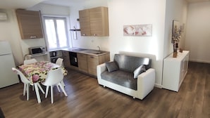 A compact kitchen with wooden cabinets, a dining area with a floral tablecloth, and a grey sofa. - Francy's House, just minutes from the Vatican (Roma)