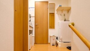 Un corridoio stretto con pavimento in legno, una porta chiusa in fondo e un piccolo tavolo bianco con alcuni oggetti sopra.