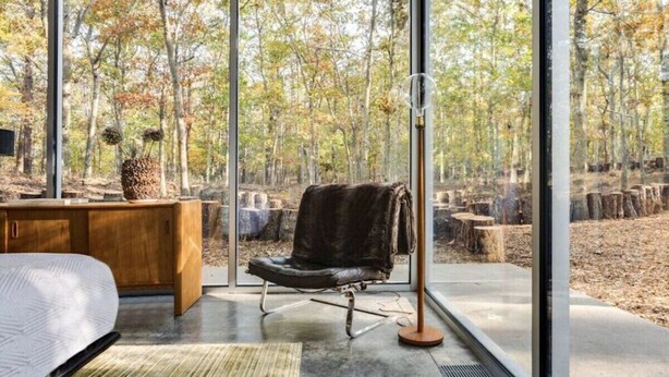 Une chambre moderne dotée d’une grande fenêtre, d’un fauteuil en cuir, d’un bureau en bois et d’un lampadaire.