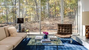 Un salon moderne avec une grande fenêtre, un canapé, un fauteuil, une table basse et un téléviseur.
