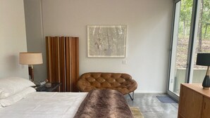 Une chambre à coucher moderne avec un grand lit, un fauteuil en cuir capitonné, une armoire en bois et une grande fenêtre.